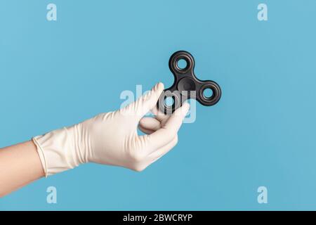 Profil Seitenansicht Nahaufnahme der menschlichen Hand in weißen OP-Handschuhe mit schwarzem Fidget Spinner. Indoor, Studio-Aufnahme, isoliert auf blauem Hintergrund. Stockfoto