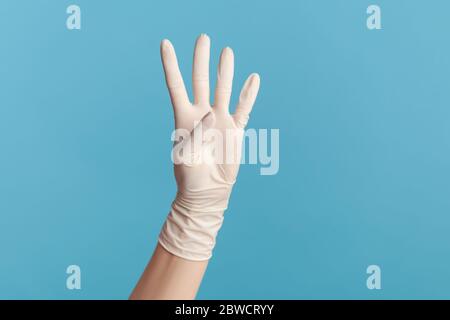 Profil Seitenansicht Nahaufnahme der menschlichen Hand in weißen OP-Handschuhe zeigt Nummer vier 4 mit der Hand. Indoor, Studio-Aufnahme, isoliert auf blauem Hintergrund. Stockfoto