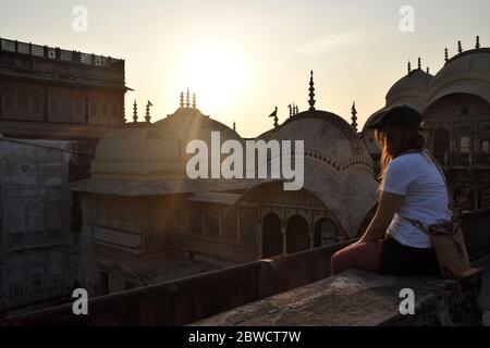 Alleinreisende, eine junge Frau in den 20er Jahren, auf dem Dach sitzend und genießt den Sonnenuntergang über der Stadt. Foto aufgenommen in Indien. Stockfoto