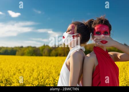 Zwei schöne junge Brünette Mädchen mit kreativen hellen Make-up in Tuniken auf einem Hintergrund von einem Feld von gelben Blumen und blauen Himmel. Ein Mädchen in einer Maske Stockfoto