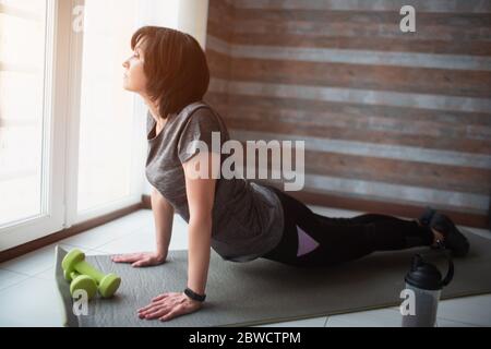 Erwachsene fit schlanke Frau hat Training zu Hause. Seitenansicht des Senior-Modells, das auf den Knien steht und den Körper auf der Matte hält. Stretching ihren Körper trainieren und Stockfoto
