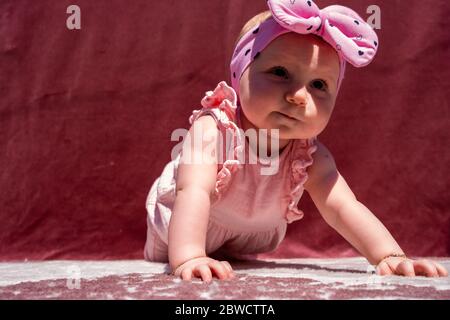 Nettes Baby Mädchen tragen liebenswert Hut tun Push-up im Freien, Blick auf die Kamera und lächelnd auf rotem Hintergrund Stockfoto