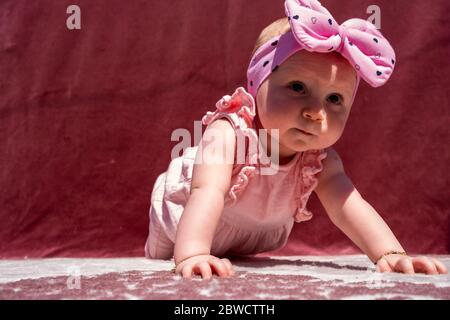 Nettes Baby Mädchen tragen liebenswert Hut tun Push-up im Freien, Blick auf die Kamera und lächelnd auf rotem Hintergrund Stockfoto