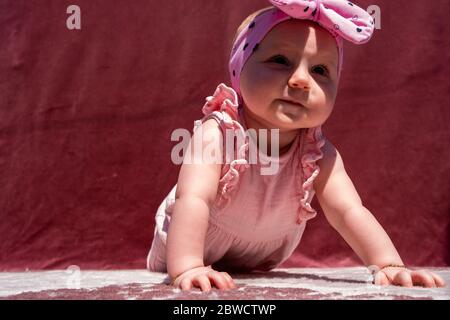 Nettes Baby Mädchen tragen liebenswert Hut tun Push-up im Freien, Blick auf die Kamera und lächelnd auf rotem Hintergrund Stockfoto