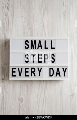 „kleine Schritte jeden Tag“, Worte auf einem Leuchtkasten auf einer weißen Holzfläche, Draufsicht. Über Kopf, von oben, flach gelegt. Stockfoto