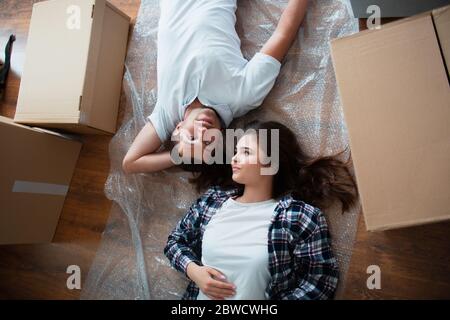 Ein junges Ehepaar im Wohnzimmer im Haus liegt auf dem Boden in der Nähe von Kartons. hey sind glücklich über neue Heimat. Umzug, Kauf eines Hauses Stockfoto
