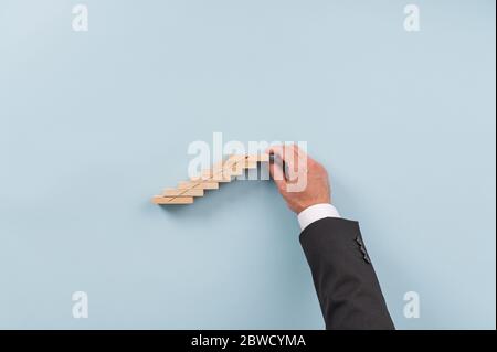 Hand eines Geschäftsmannes, der Treppe aus Holzpflöcken mit einem nach oben zeigenden Pfeil baut. Konzeptionelles Bild der Geschäftsvision und des Startup. Stockfoto