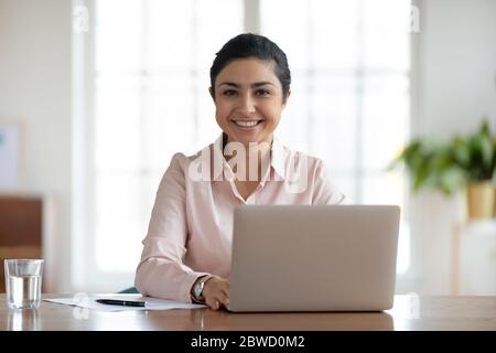 Junge lächelnde indische Frau sitzt am Tisch mit Computer. Stockfoto