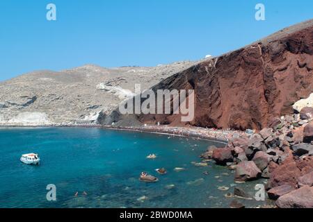 Touristen schwimmen und genießen die Sonne am Roten Strand von Santorini unter der roten Vulkanklippe Stockfoto