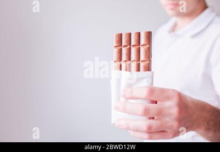 Junger Mann in weißem Hemd isoliert über Hintergrund. Guy halten leckere süße Schokolade in der Hand und Pose vor der Kamera. Leckere leckere leckere leckere Süßigkeiten. Stockfoto