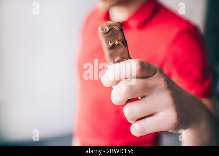 Junger Mann in rotem Hemd isoliert auf weißem Hintergrund. Nahaufnahme Hand hält Swet Snack. Leckere leckere Schokolade. Stockfoto