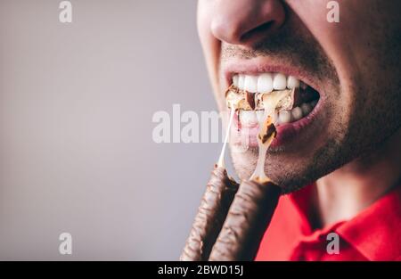 Junger Mann in rotem Hemd isoliert über Hintergrund. Nahaufnahme Bild von Kerl mit geöffnetem Mund und gebissene Bar in ihm. Leckeres Essen. Stockfoto