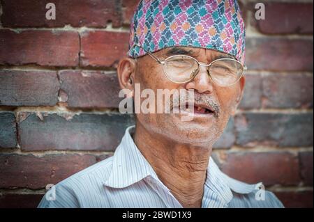 PATAN, LALITPUR, NEPAL - 15. AUGUST 2018: Ein nicht identifizierter Newari älterer Mann sitzt vor dem Königspalast von Mul Chowk auf dem Patan Durbar Square in Nepal Stockfoto