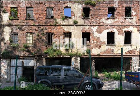 Alte Adandoned Ruine Gebäude Backsteinmauer mit Bäumen auf der Steinmauer und Auto daneben gewachsen Stockfoto