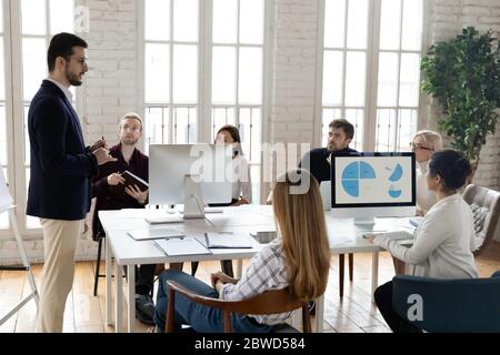 Selbstbewusster männlicher Teamleiter erklärt Kollegen mit unterschiedlichen Rassen die Marketingstrategie. Stockfoto