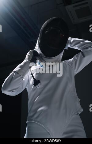 Niedrige Winkelansicht des Fechters, der auf die Fechtmaske aufsetzt Stockfoto