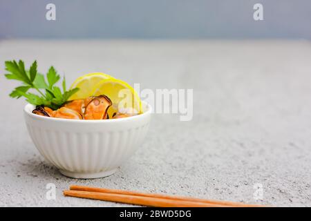 Muscheln ohne Schale mit Zitronenscheiben in weißer Keramikschale. Meeresfrüchtekonzept. Selektiver Fokus. Platz für Text Stockfoto