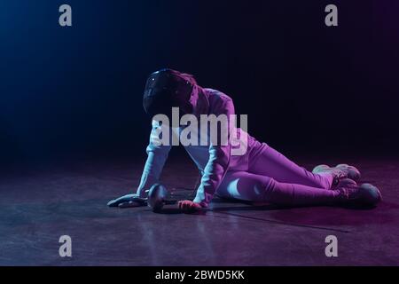 Schwertwoman in Fechtanzug und Maske hält Vergewaltiger während auf dem Boden auf schwarzem Hintergrund sitzen Stockfoto