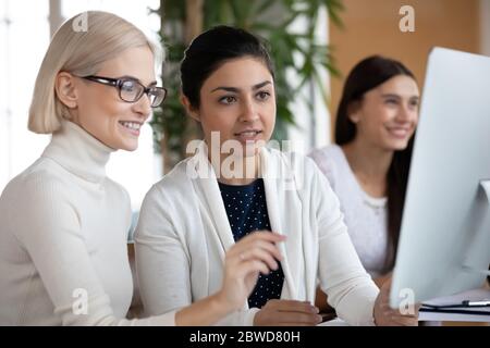 Lächelnde Geschäftsfrau in Brillen, die Projektdetails mit einem indischen Kollegen diskutiert. Stockfoto