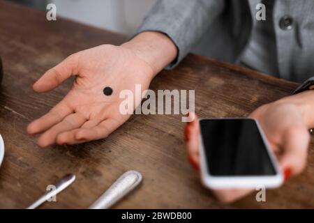 Cropped Ansicht der Frau mit schwarzem Punkt auf der Handfläche halten Smartphone mit leerem Bildschirm, häusliche Gewalt Konzept Stockfoto