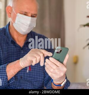 Paris, Frankreich - März 2020: Älterer Mann trägt während der weltweiten Coronavirus-Einengung Plastikschutzhandschuhe und chirurgische medizinische Atemmaske mit dem Apple iPhone 11 Pro Smartphone Stockfoto