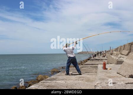 Fischer werfen die Angelschnur und Fischer ruhen an der Küste mit Mate (Argentinischer Tee) neben einigen Stängeln an der Front und auf dem Rücken Stockfoto