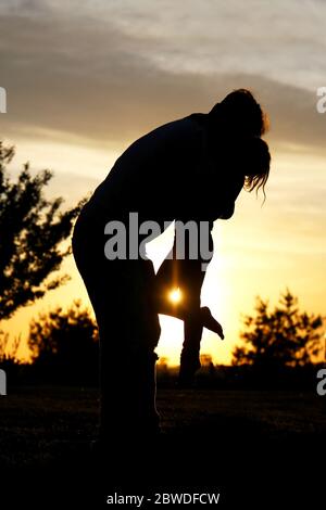 Eine Silhouette eines liebevollen Vaters nimmt seine junge Tochter draußen bei Sonnenuntergang an einem Sommertag auf und umarmt sie. Stockfoto