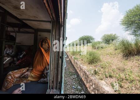 Frau mit Blick aus fahrenden Zug Fenster, zweite Klasse Zug. Indian Railways. Indien. Stockfoto