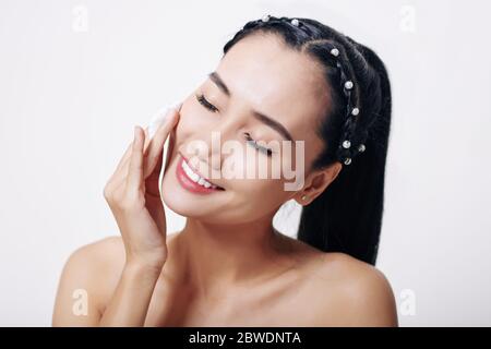 Lächelnd ziemlich junge vietnamesische Frau Anwendung feuchtigkeitsspendende Lotion auf ihr Gesicht Stockfoto