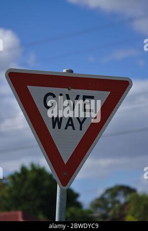 Nahaufnahme von Give Way Zeichen in roter Dreiecksform und blauem Himmel Hintergrund Stockfoto