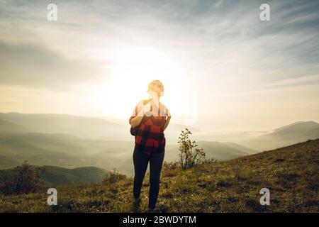 Junge Frau Traveler In Red Plaid Shirt Mit Rucksack Klettert Bergauf Bei Sonnenaufgang. Scout Travel Adventure Konzept Stockfoto