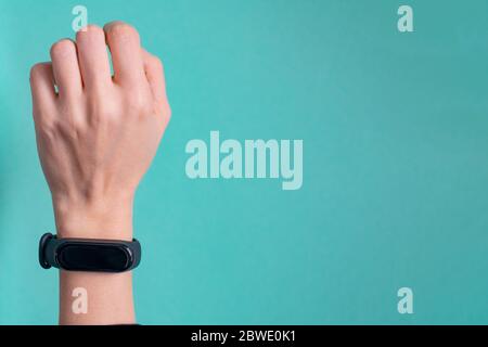 Schwarzes Fitness Armband für Sporttraining auf einer Mädchenhand auf mintblauem Hintergrund. Selektiver Fokus. Stockfoto