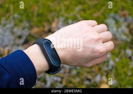 Schwarzes Fitness Armband für Sporttraining auf einer Mädchenhand auf natürlichem Hintergrund. Sport im Wald. Selektiver Fokus. Stockfoto