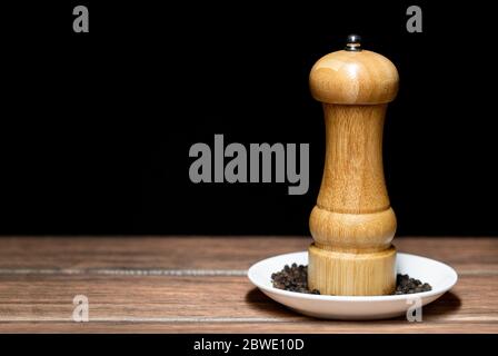 Schwarze Pfeffermühle mit Pfefferkörnern auf einer weißen Keramikplatte Nahaufnahme dunkles Essen Stockfoto