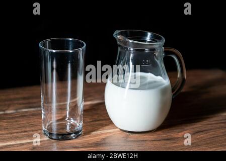 Eine leere Glasschale und ein Glas Kuhmilch auf einem Holztisch und schwarzem Hintergrund Stockfoto