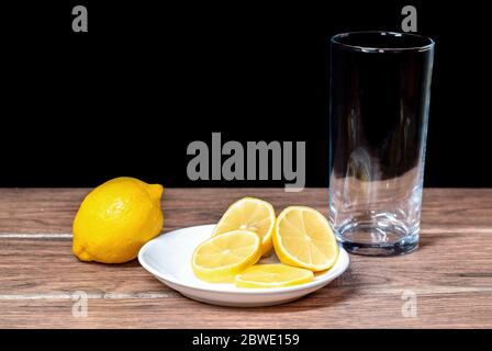 Zitronen mit Scheiben Zitronenstücke auf einer Keramikplatte und einem Glas hinter schwarzem Hintergrund Stockfoto