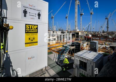 Ein Bauarbeiter passiert die Coronavirus-Hinweisschilder im Kernkraftwerk Hinkley Point C in der Nähe von Bridgwater, Somerset, Europas größter Baustelle, wo er einen Betoneinlauf in den Sockel des Kernreaktors Block 2 fertigstellt. Stockfoto