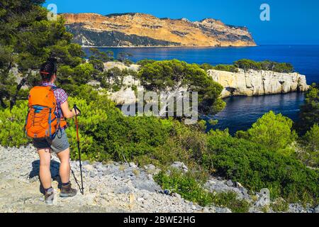 Sportliche Wandererin mit Rucksack, die die Aussicht mit der blauen Wasserbucht vom Wanderweg im Calanques Nationalpark, Cassis, Provence, Frankreich, EUR genießt Stockfoto