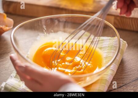 Detail der Eier, die in einer Schüssel auf einem Handtuch und Holztisch gelegt Whisked Stockfoto