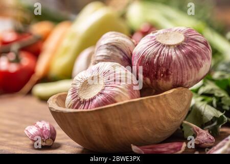 Knoblauchköpfe in Holzschüssel, umgeben von Gemüse Stockfoto