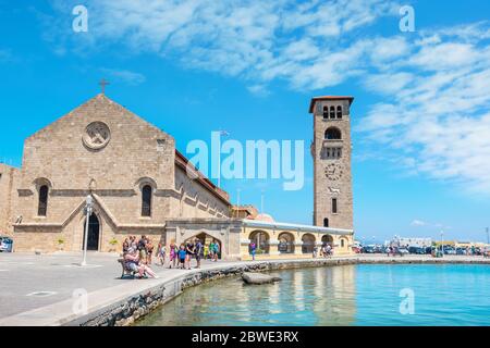 Touristen, die auf einem Kai des Mandraki Hafens in der Nähe der Evangelismos (Verkündigung) Kirche in Rhodos spazieren. Griechenland Stockfoto