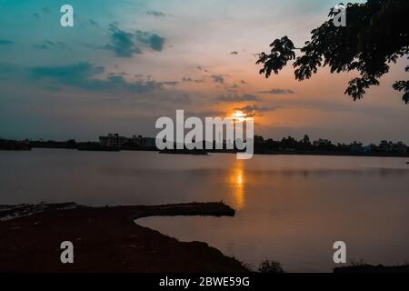 Ein schöner Sonnenaufgang in der Nähe eines Sees.Himmel mit Wolken und Sonne gefüllt ist, piepst aus ihm heraus.die Reflexion von ihm kann auf Wasser gesehen werden Stockfoto