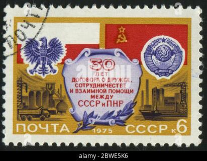 RUSSLAND - UM 1975: Briefmarke gedruckt von Russland, zeigt Flaggen und Waffen von Polen und der UdSSR, Fabriken, um 1975. Stockfoto