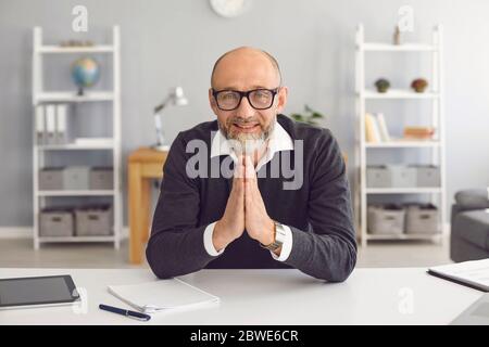 Selbstbewusster älterer männlicher Geschäftsmann, der die Kamera ansieht, sagt, dass eine Online-Webanwendung in einer Wohnung sitzt. Stockfoto