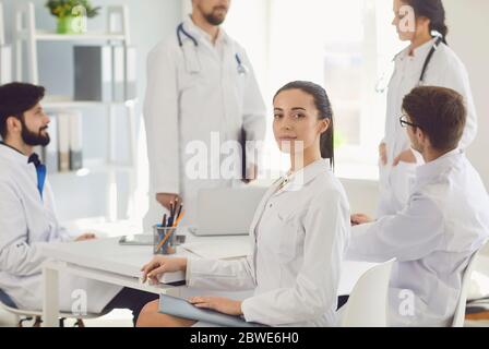 Ärztin sitzt an einem Tisch mit Kollegen in weißen Labormänteln in einem medizinischen Krankenhaus. Stockfoto