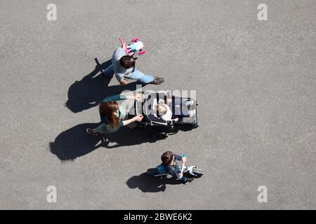 Pärchen mit Kindern, die auf einer Straße in der Stadt spazieren gehen, von oben gesehen. Eltern mit kleinen Sohn im Fahrrad und Tochter im Kinderwagen, Konzept der Familienfreizeitgestaltung Stockfoto