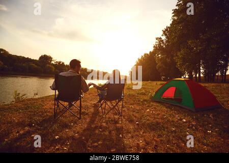 Ein Wanderer Paar Hände halten neben einem Zelt am See bei Sonnenuntergang. Stockfoto