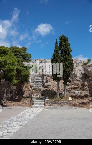Athen, Griechenland. Steintreppe zum Areopagus Hügel, griechische Zypressen, blauer Himmel in einem sonnigen Frühlingstag, vertikales Foto Stockfoto
