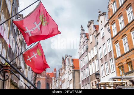 Danzig, Polen - 12. April 2019; Flaggen mit dem Wappen von Danzig auf dem Hintergrund von bunten Häusern Stockfoto