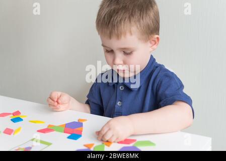 Niedlicher Junge spielt Holz Spiel Tangram. Kreative und pädagogische Spiele auf Quarantäne. Kopierbereich Stockfoto